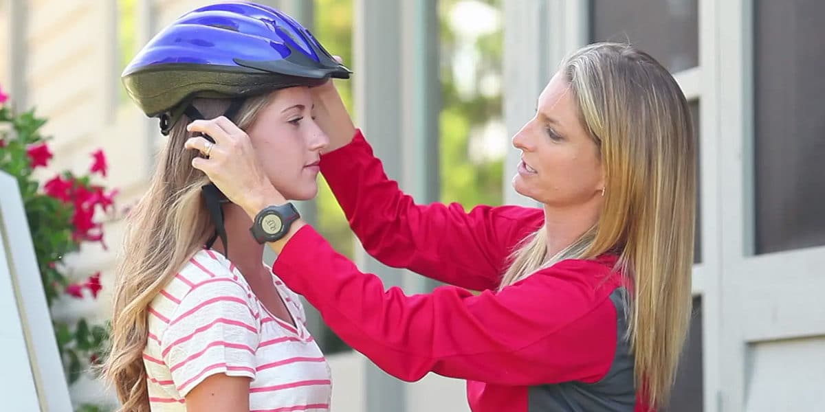 Mother helping secure teen daughter's bike helmet